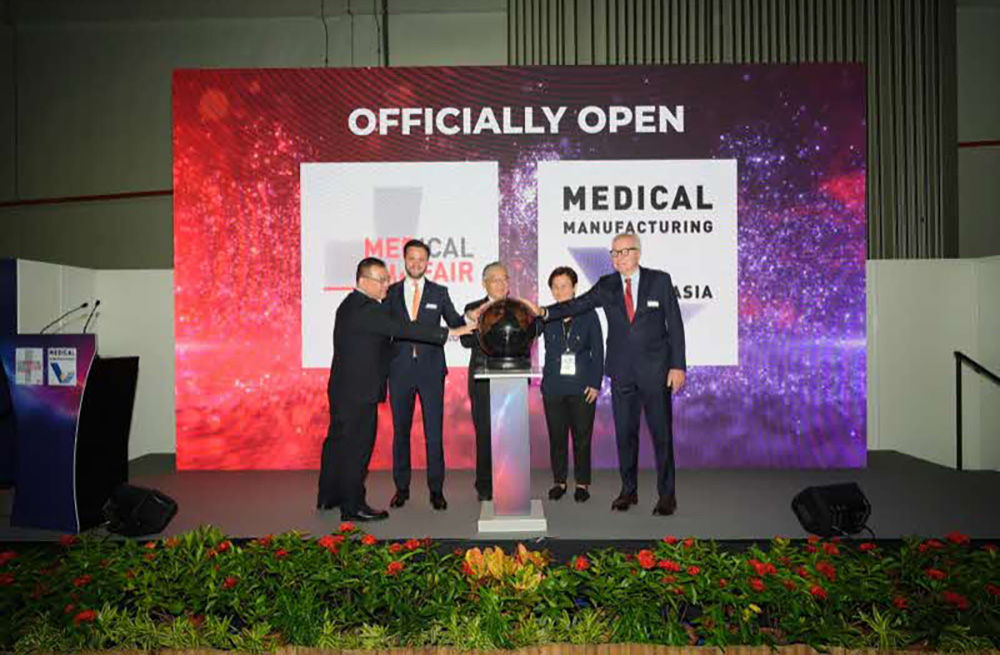 Five leaders celebrate the opening of Medical Fair Asia, standing around a podium with a dark sphere, set against a vibrant backdrop.